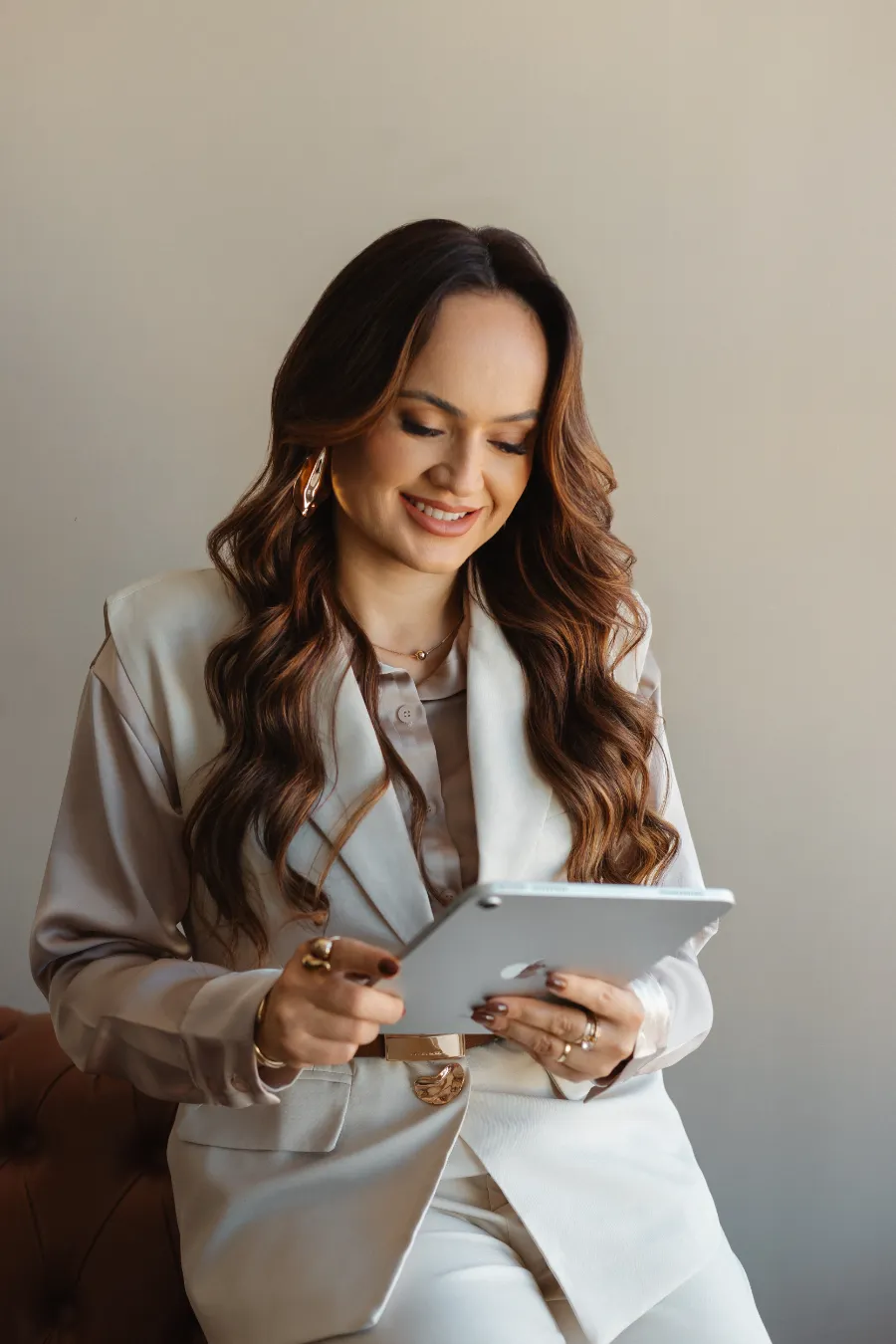 Nathaly de terninho creme, sorrindo enquanto olha um tablet.